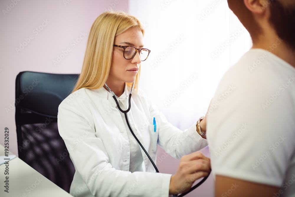 Doctor examining patient with stethoscope in medical office. Doctor using stethoscope to exam man patient heart. Portrait of female doctor examines a patient with stethoscope. Doctor examining patient with stethoscope in medical office. Doctor using stethoscope to exam man patient heart. Portrait of female doctor examines a patient with stethoscope.