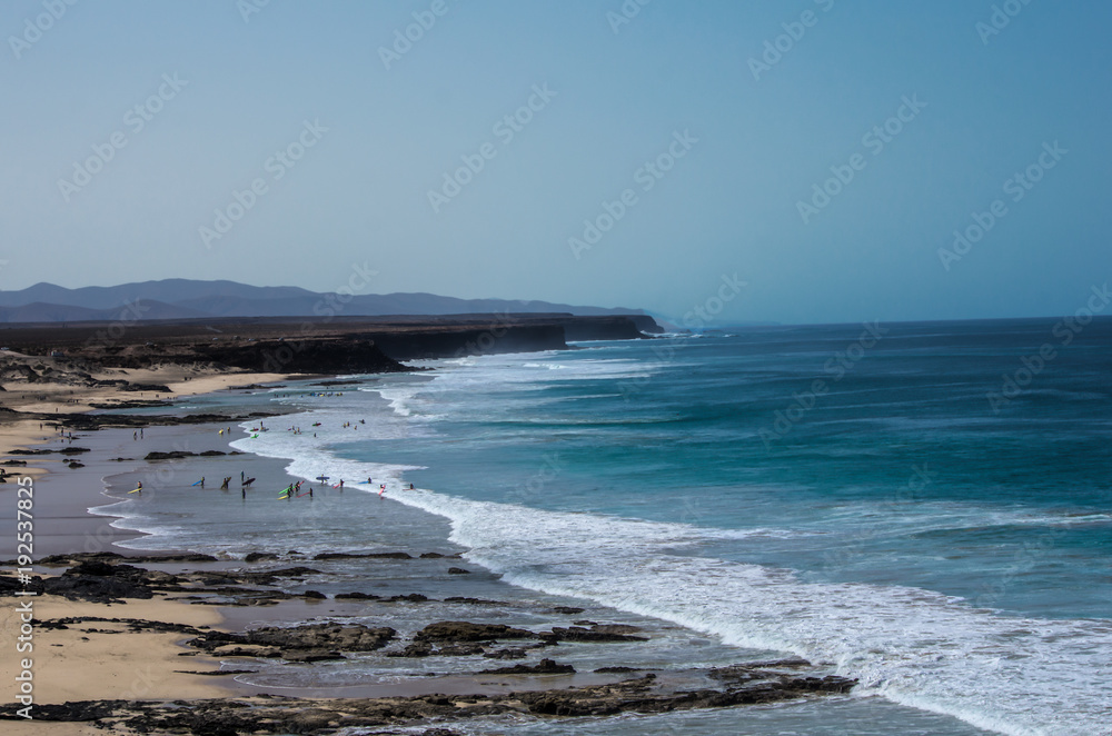 surfers waiting for the waves on the long sandy beach of Fuerteventura, Spain