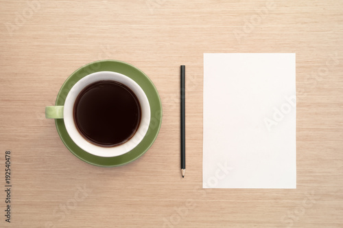 A green cup of coffee on the background of a table and a white shee and pencil