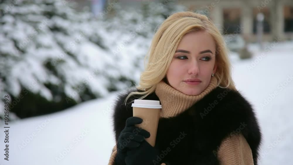 Portrait of a thoughtful beautiful girl in a beige sweater and a black coat with a Cup of coffee in a snowy city Park. Portrait of a thoughtful beautiful girl in a beige sweater and a black coat with a Cup of coffee in a snowy city Park.