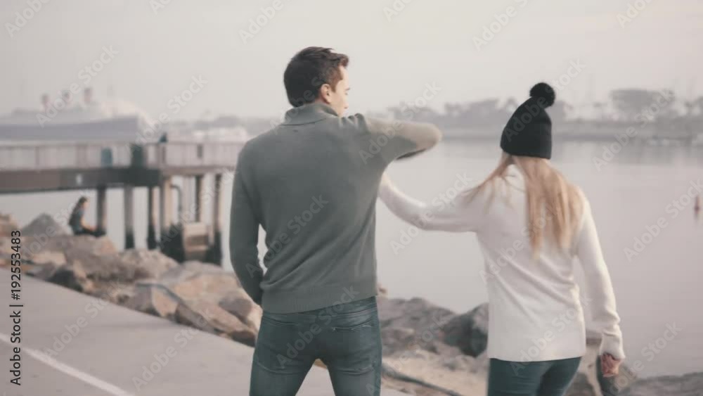 Loving couple of young people are walking in the park. Against the background of a beautiful bay. Pleasant evening near the ocean. Talking and kissing. Steadicam shooting. View from the back. Loving couple of young people are walking in the park. Against the background of a beautiful bay. Pleasant evening near the ocean. Talking and kissing. Steadicam shooting. View from the back.