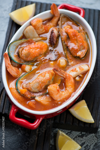 Close-up of seafood soup or french buyabes in a bowl on a black wooden serving board, selective focus, vertical shot