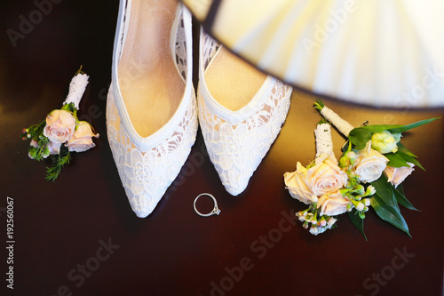 Wedding attributes of the bride. View from above. Beautiful and delicate white shoes with boutonniks and a ring photo