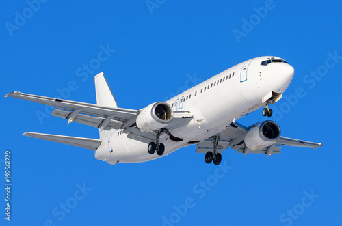Passenger airplane with the chassis released before the landing at the airport against the blue sky.