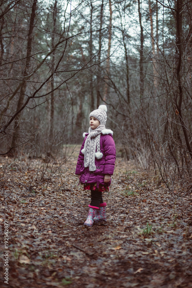 A little girl is standing in a forest on a path. A little girl is standing in a forest on a path.