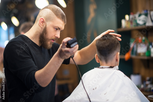 the young man the hairdresser cuts the schoolboy in hairdressing salon