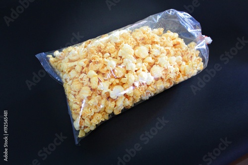 Sweet popcorn in transparent plastic bag, black background
