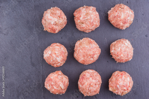 Raw meatballs on a slate board, dark background, top view - copy space for a recipe