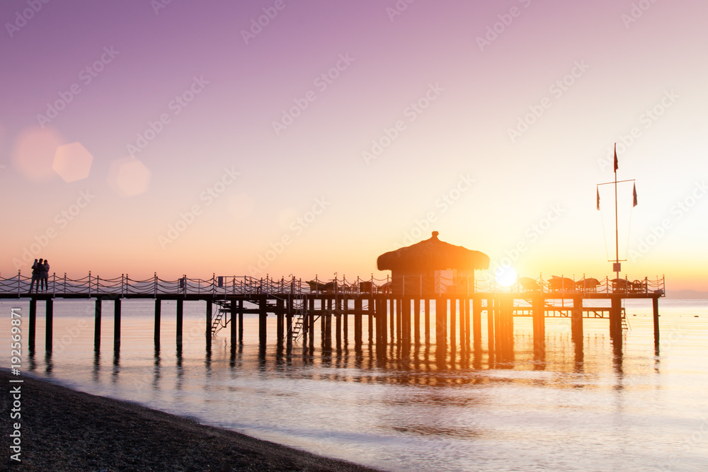 The bungalow on the pier is flooded with sunlight. Lilac from the dawn sky.