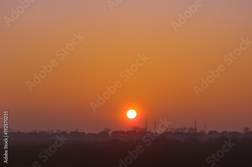 the setting sun over the roofs of houses. a haze over the field. natural background.