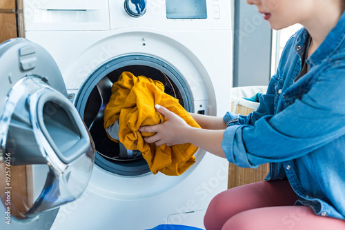 cropped shot of young woman putting laundry into washing machine photo