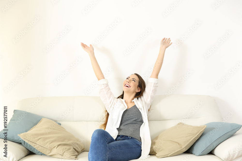 Happy woman raising arms and looking above on a couch Happy woman raising arms and looking above on a couch