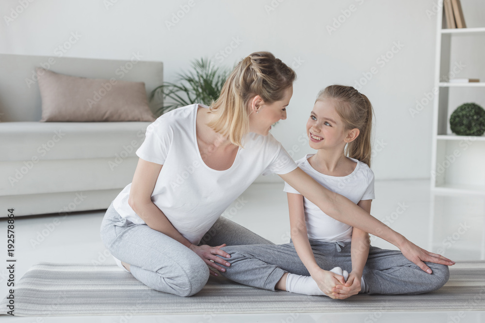 mother teaching daughter how to sit in yoga butterfly pose