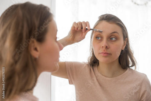 Portrait of attractive young woman putting on makeup at home. Eyebrow brush