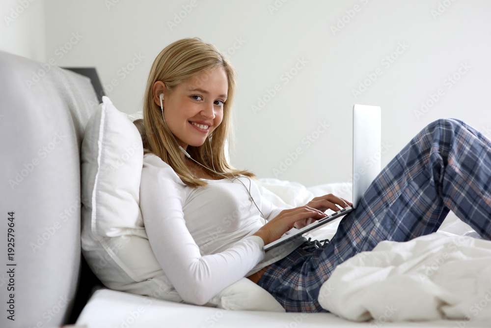 Hübsche blonde Frau mit Kopfhörer und Laptop in ihrem Bett lacht Hübsche blonde Frau mit Kopfhörer und Laptop in ihrem Bett lacht