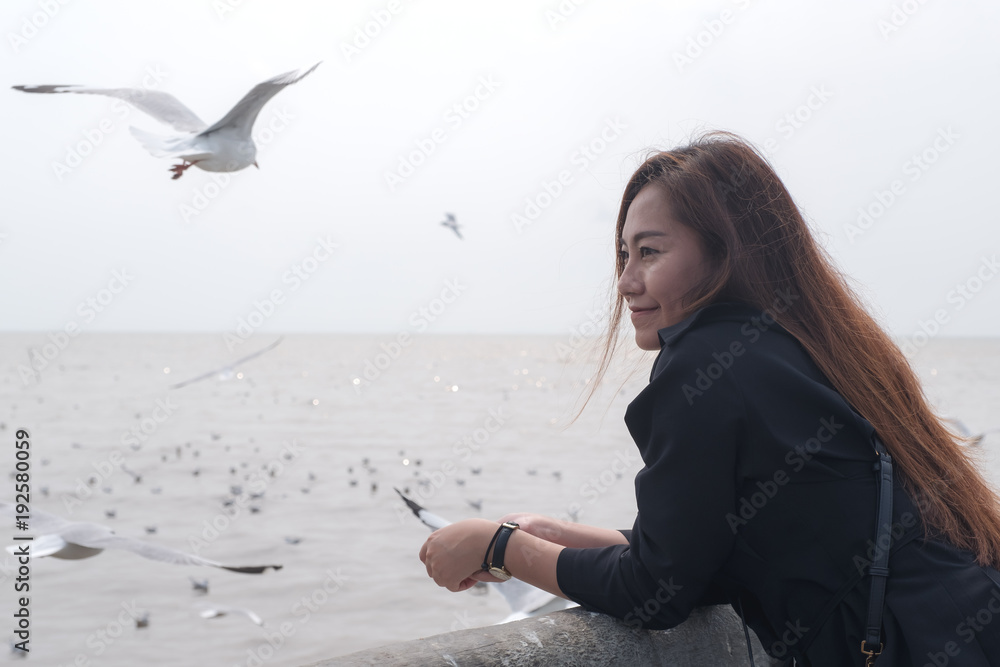 Closeup image of a beautiful asian woman with a flock of seagulls flying above the sea with clear sky background
