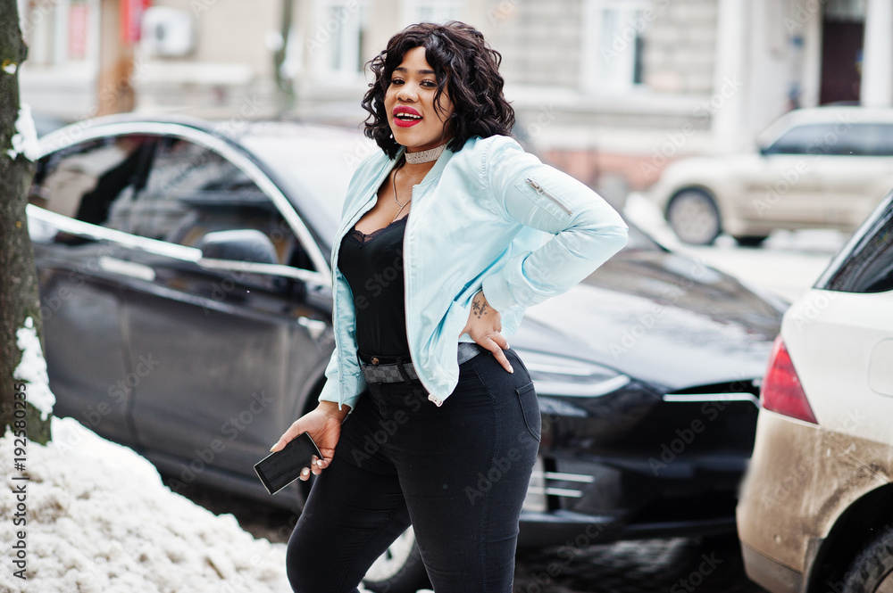 Stylish african american plus size model with mobile phone against electro car.