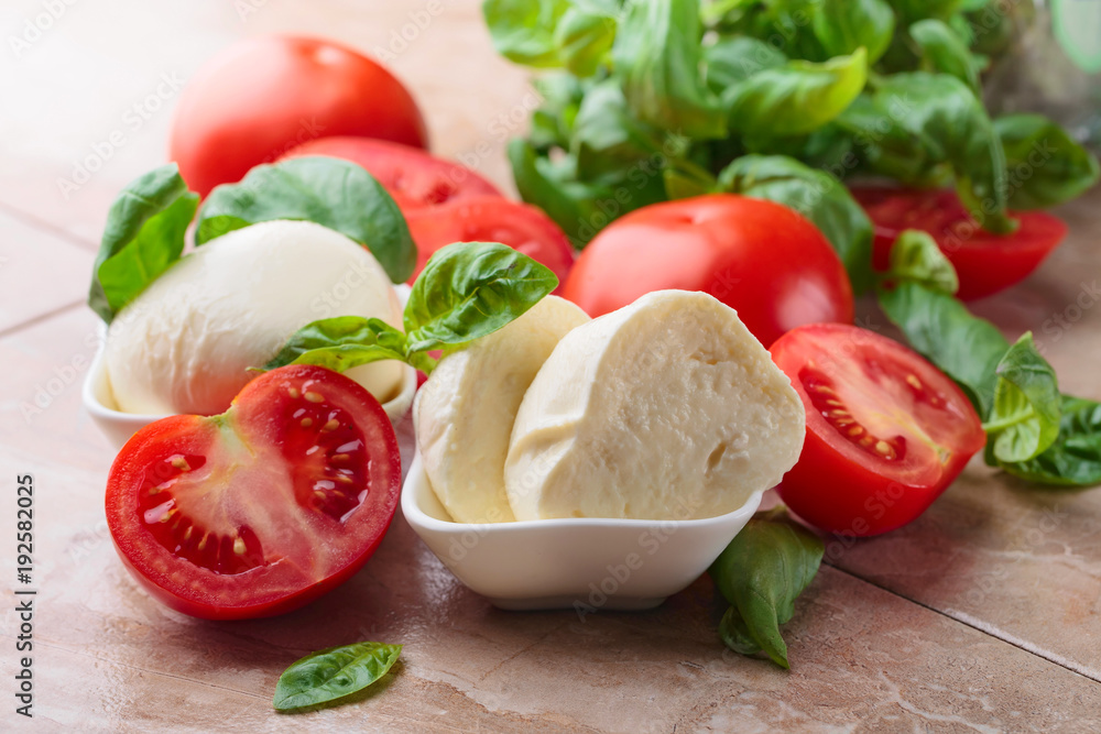  Mozzarella cheese with tomatoes and green basil on a kitchen table .