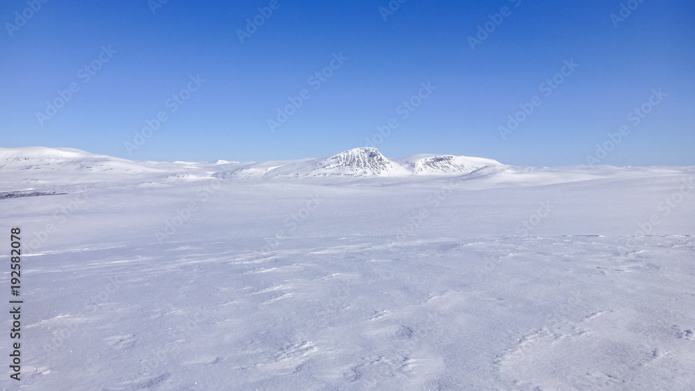 Large open field with snow and mountains on the horizon in northern Sweden near the polar circle.