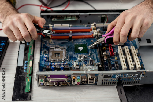 cropped image of hands with tongs fixing motherboard of pc