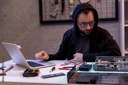 man in hoodie using laptop while looking on broken pc
