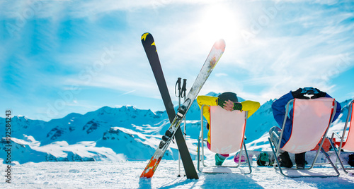 Image from back of vacationers in armchair, skis, sticks in snowy resort photo