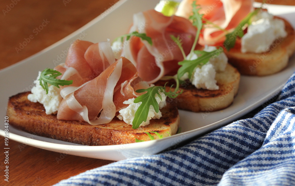 Bruschetta with ricotta, prosciutto, rucola on white plate Bruschetta with ricotta, prosciutto, rucola on white plate
