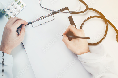 The doctor writes, large hands, near a stethoscope in the hospital