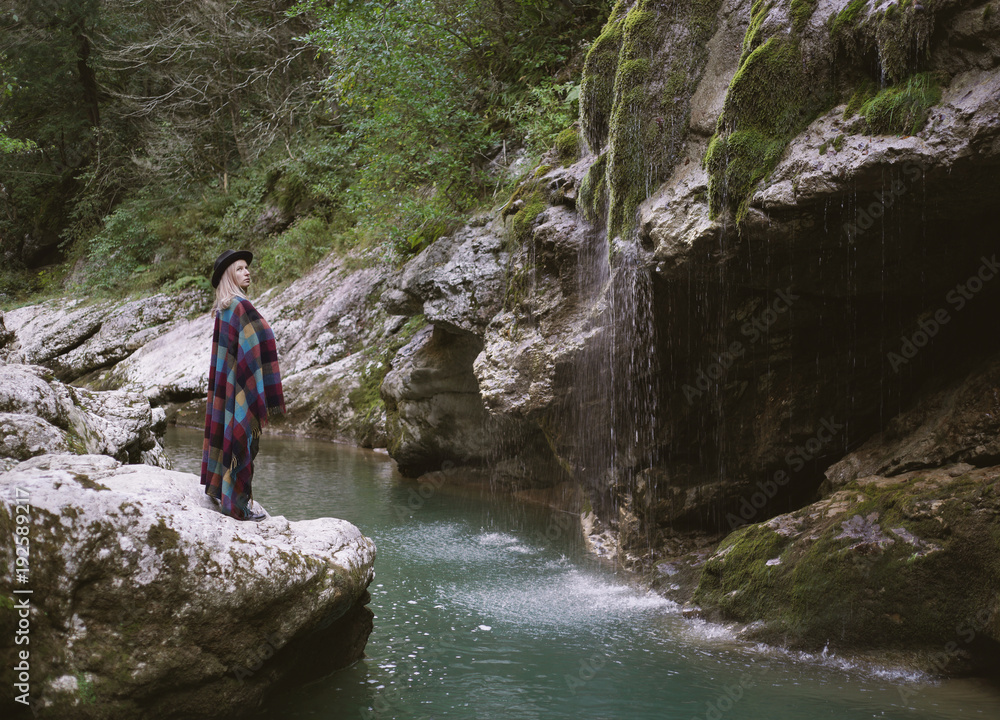 Young woman in poncho standing close mountain river.