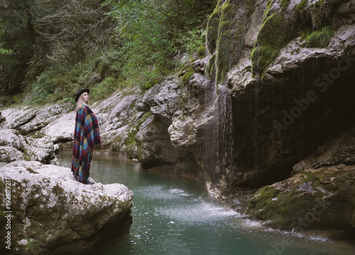 Young woman in poncho standing close mountain river.