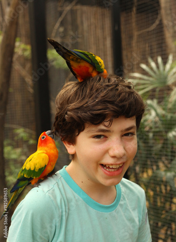 Photography teenager smiling boy in asian zoo with ara parrots on his head