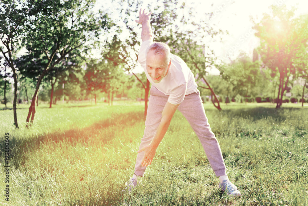 Ready for exercises. Optimistic elderly man doing exercises in fresh air while being excited and pleased
