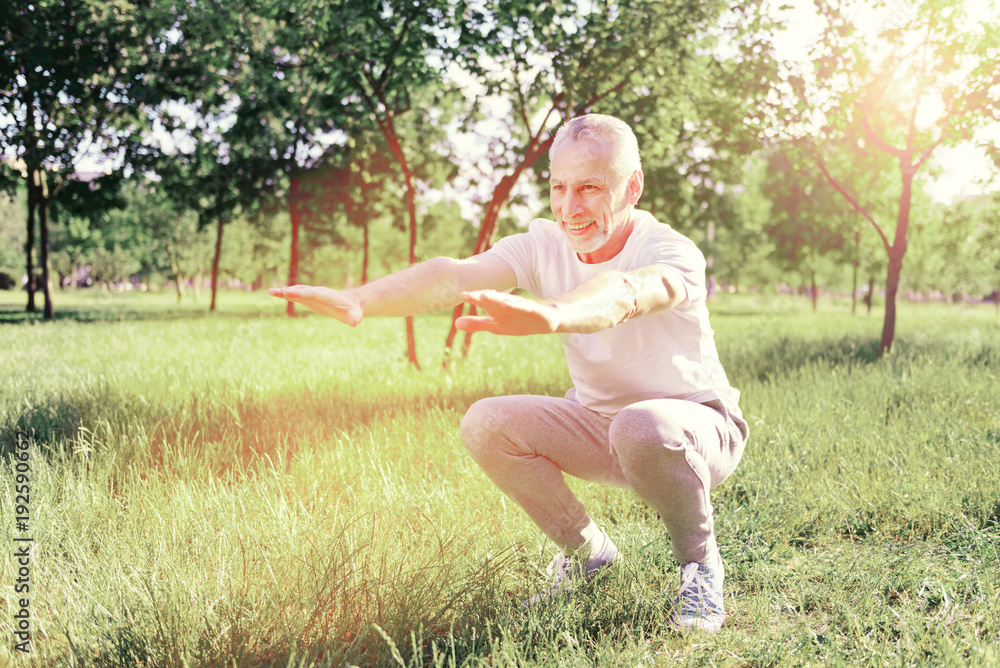 Pleasant day. Full length of elderly man looking away while doing useful exercises outdoors Pleasant day. Full length of elderly man looking away while doing useful exercises outdoors