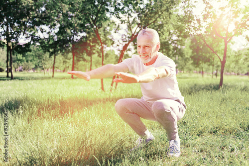 Pleasant day. Full length of elderly man looking away while doing useful exercises outdoors