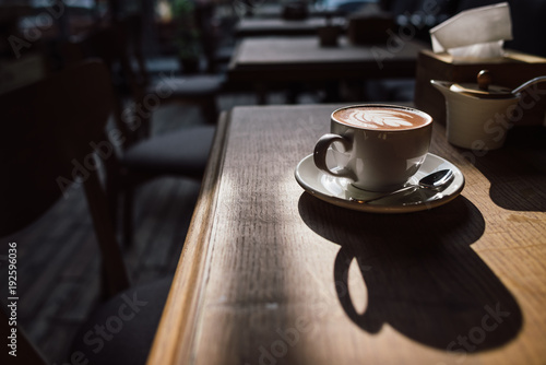 A cup of coffee on the wood table and sunlight with cozy cafe interior background