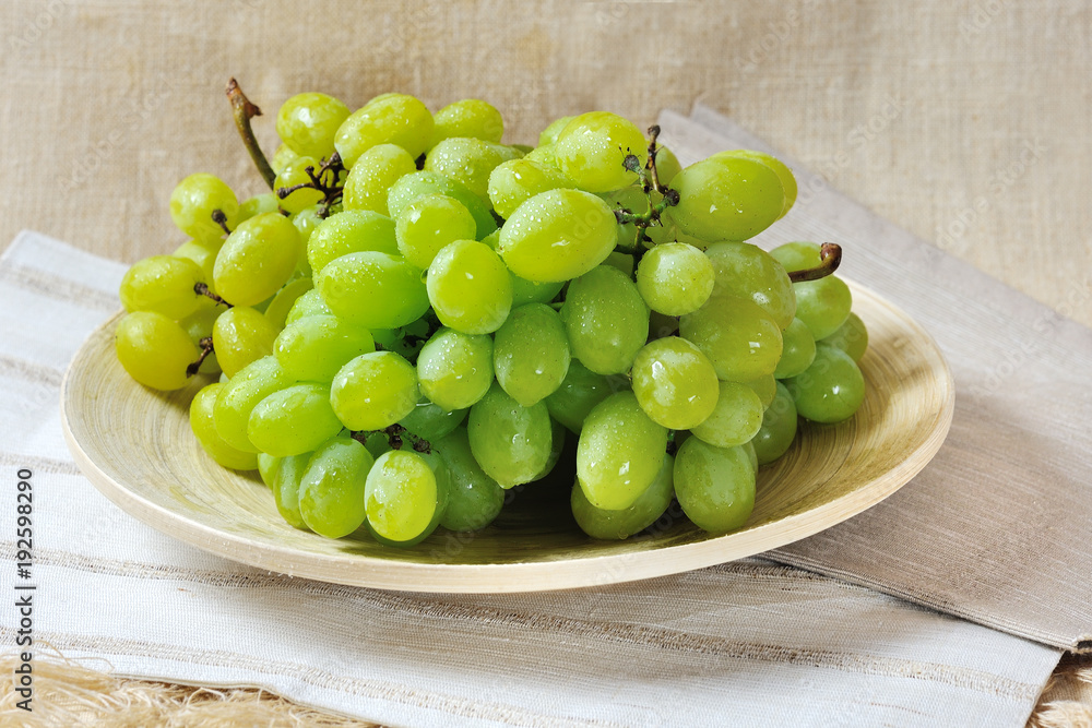 Bunch of sweet juicy green grapes on a wooden plate Bunch of sweet juicy green grapes on a wooden plate