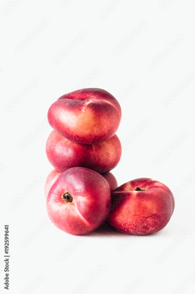 Stack of fresh flat donut nectarines, red saturn nectarines or ripe fuzzless vineyard peaches on white background