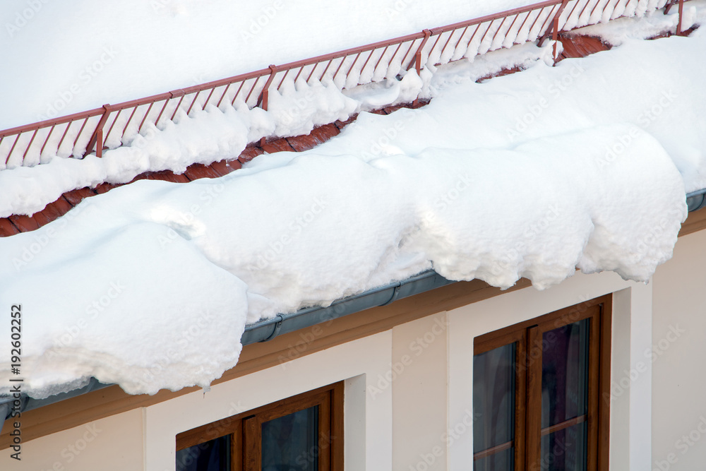 Fototapeta premium Snow overhangs dangerously from the roof of the house. Snow melting on the roof of the house.