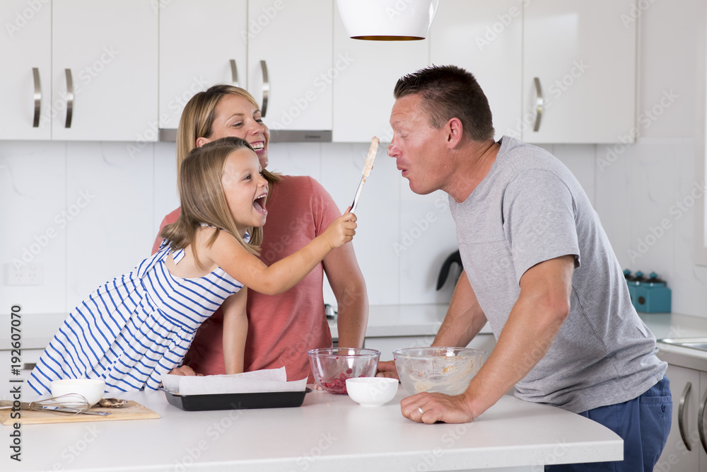 Fototapeta premium young happy couple baking together with little young beautiful daughter at home kitchen having fun playing with cream in family lifestyle