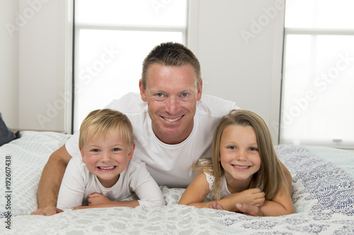 young man lying on bed together with her little sweet 3 and 7 years old son and daughter playing happy in family father children love lifestyle