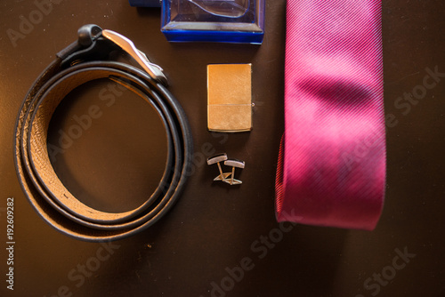 Groom’s accessories: golden cufflinks, cigarette Lighter, black leather belt and a red necktie out of focus