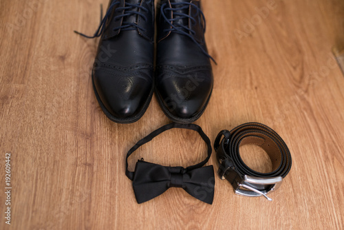 The groom's wedding accessories. Black leather belt, black necktie and black shoes on a wooden background.