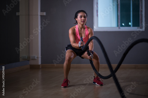 Asia women exercising with battle ropes at gym.