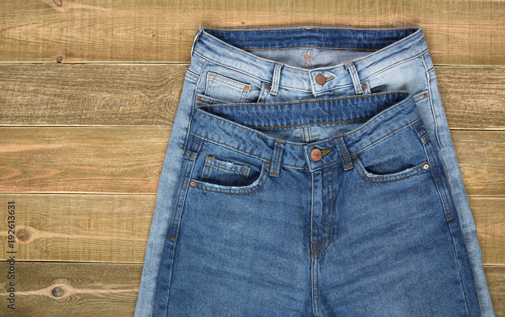 top view of two pairs of high waist women jeans front view on brown wooden background. jeans shop. top view of two pairs of high waist women jeans front view on brown wooden background. jeans shop.