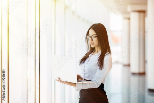 Portrait of young business woman working holding laptop standing against panoramic window with city view Free Download Portrait of young business woman working holding laptop standing against panoramic window with city view - GFXLoad