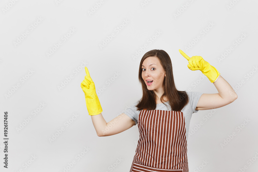 Young attractive smiling housewife in striped apron, yellow gloves isolated on white background. Beautiful housekeeper woman pointing index fingers aside looking camera. Copy space for advertisement. Young attractive smiling housewife in striped apron, yellow gloves isolated on white background. Beautiful housekeeper woman pointing index fingers aside looking camera. Copy space for advertisement.