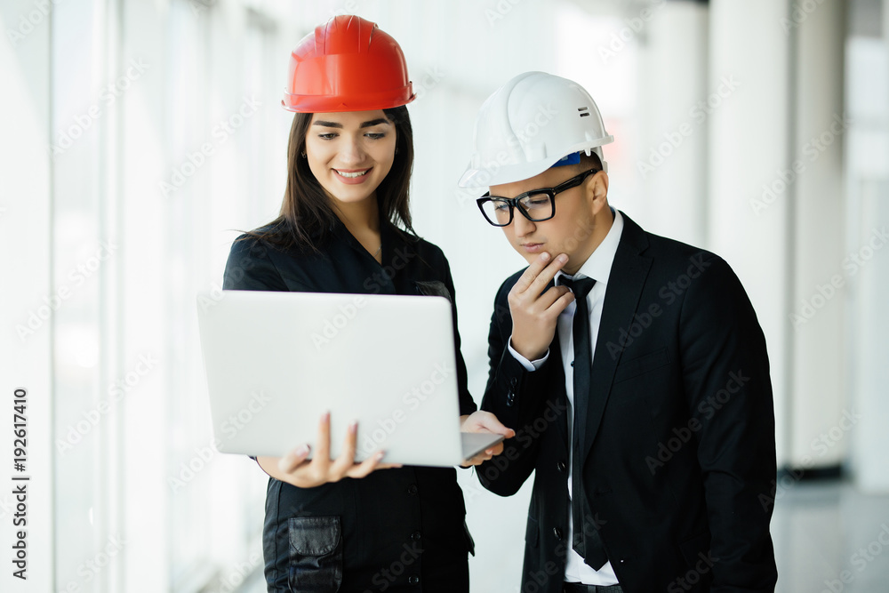 Woman and man entrepreneur and architect in hemlet at business meeting, looking at the laptop on building plans Woman and man entrepreneur and architect in hemlet at business meeting, looking at the laptop on building plans