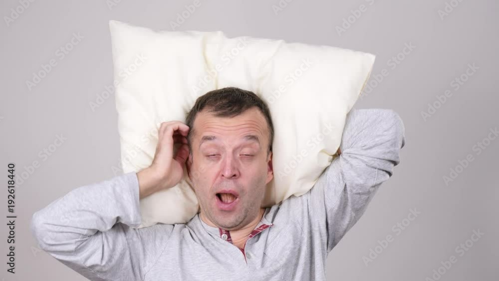 Man sleepy tired wearing nightwear holding pillow yawning. Health balance sleep deprivation concept. Male at morning with lack of slumber, on grey. Slow motion Man sleepy tired wearing nightwear holding pillow yawning. Health balance sleep deprivation concept. Male at morning with lack of slumber, on grey. Slow motion