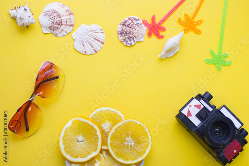 Bright yellow one-color background with slices of orange, old vintage camera, sea shells, sunglasses, top view. Travel or tourism concept. Space for a text or product display.