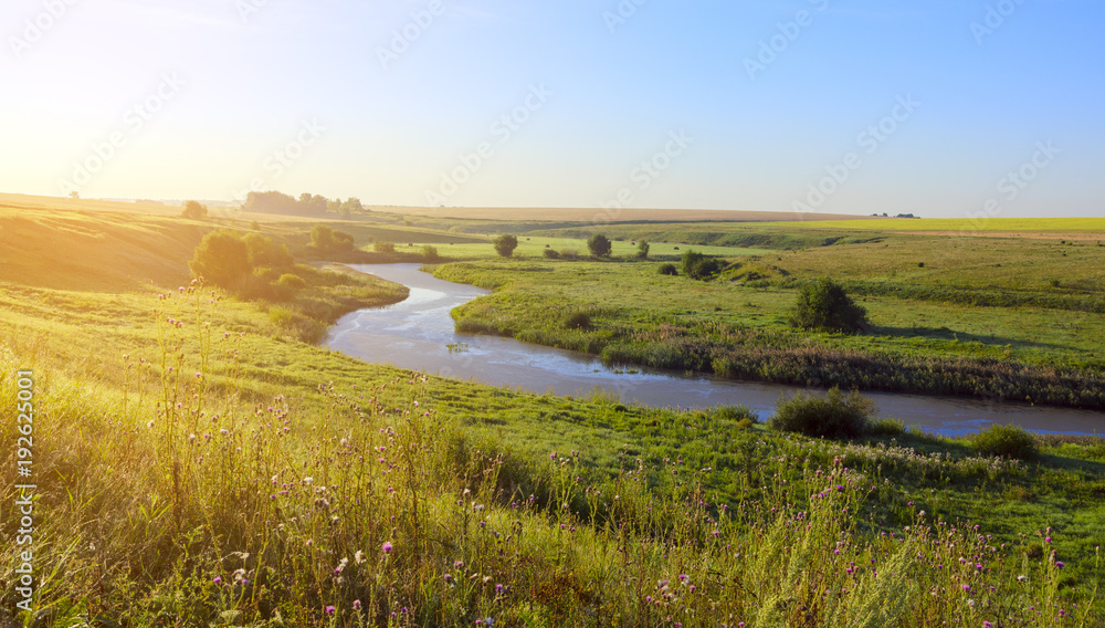 Sunny summer landscape with river.Green hills,fields and meadows.River Upa in Tula region,Russia.Sunrise.Quiet morning.Calm.Warm sunlight.Cloudless clear blue sky.